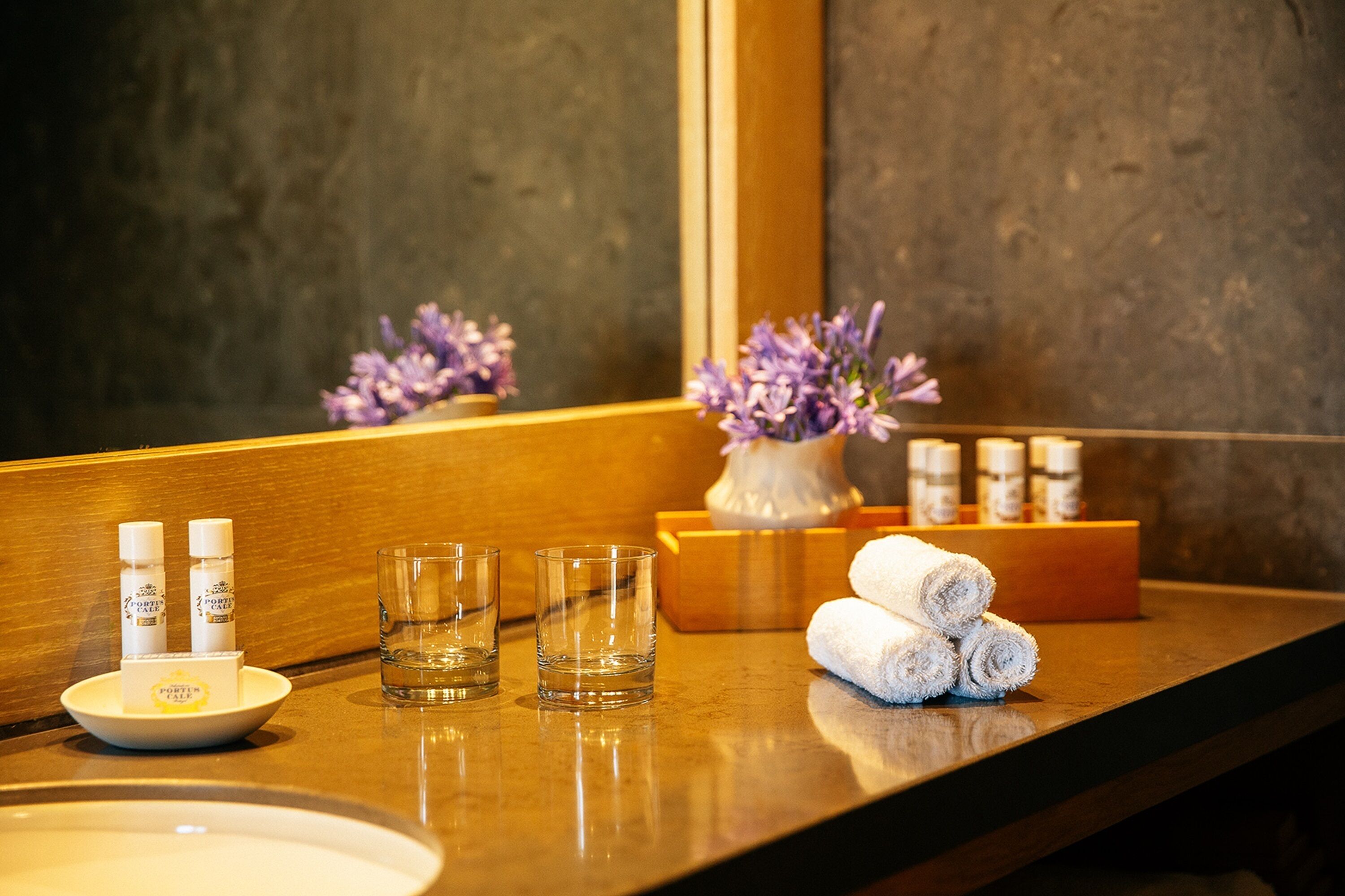 A bathroom counter with toiletries, towels, and a vase of flowers.