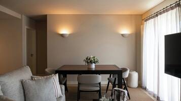 Un salon moderne comprenant un canapé, une table à manger avec des chaises, un téléviseur et une fenêtre avec des rideaux.