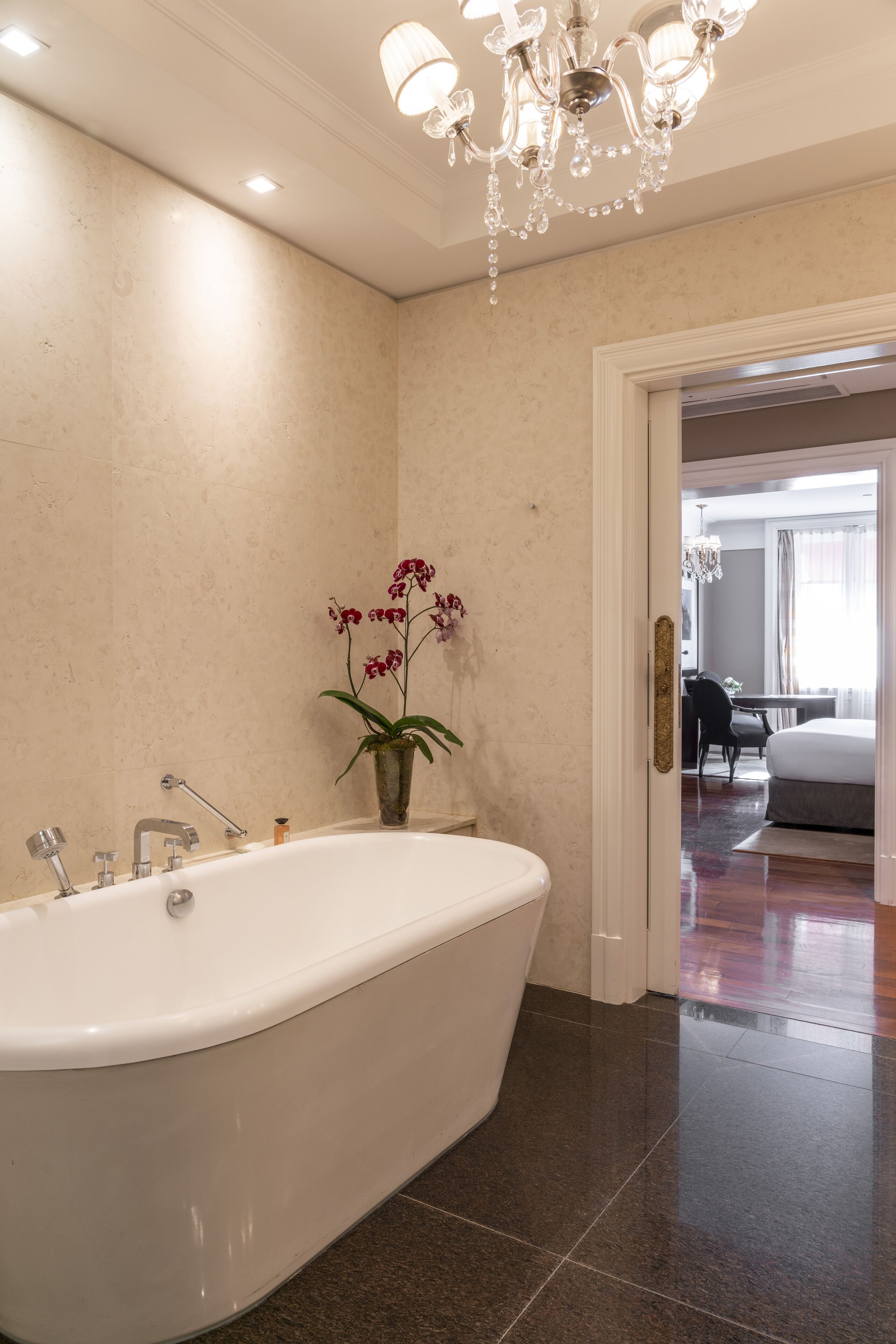 A modern bathroom with a freestanding bathtub, a chandelier, and a potted orchid.