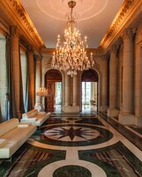 Un lobby imponente con un gran candelabro, pisos de mármol y columnas de estilo clásico.