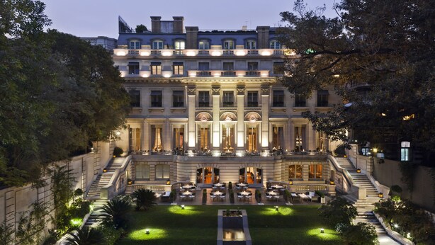 Un hotel imponente con una fachada simétrica, varios balcones y un patio iluminado con asientos al aire libre.