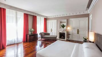 A hotel room with a large bed, a fireplace, a sofa, and a desk.