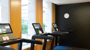 Un gimnasio con cintas de correr, un reloj de pared y una ventana con persianas.