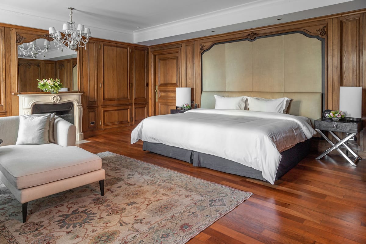 Une chambre spacieuse avec un grand lit, un coin salon avec un fauteuil, une cheminée et un lambris en bois.