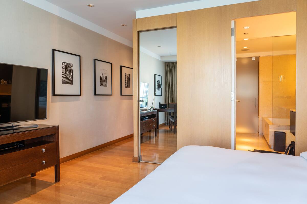 Une chambre d’hôtel moderne avec un plancher en bois, un grand lit, une télévision et des tableaux encadrés au mur.
