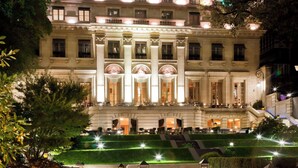 Un hotel elegante con una fachada luminosa, césped cuidado y zonas de estar al aire libre.