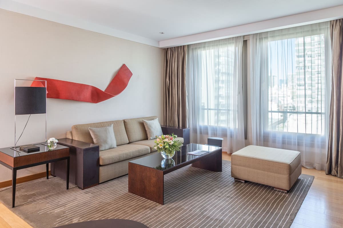Un salon moderne avec un canapé, une table basse, une table d’appoint et une grande fenêtre avec des rideaux.