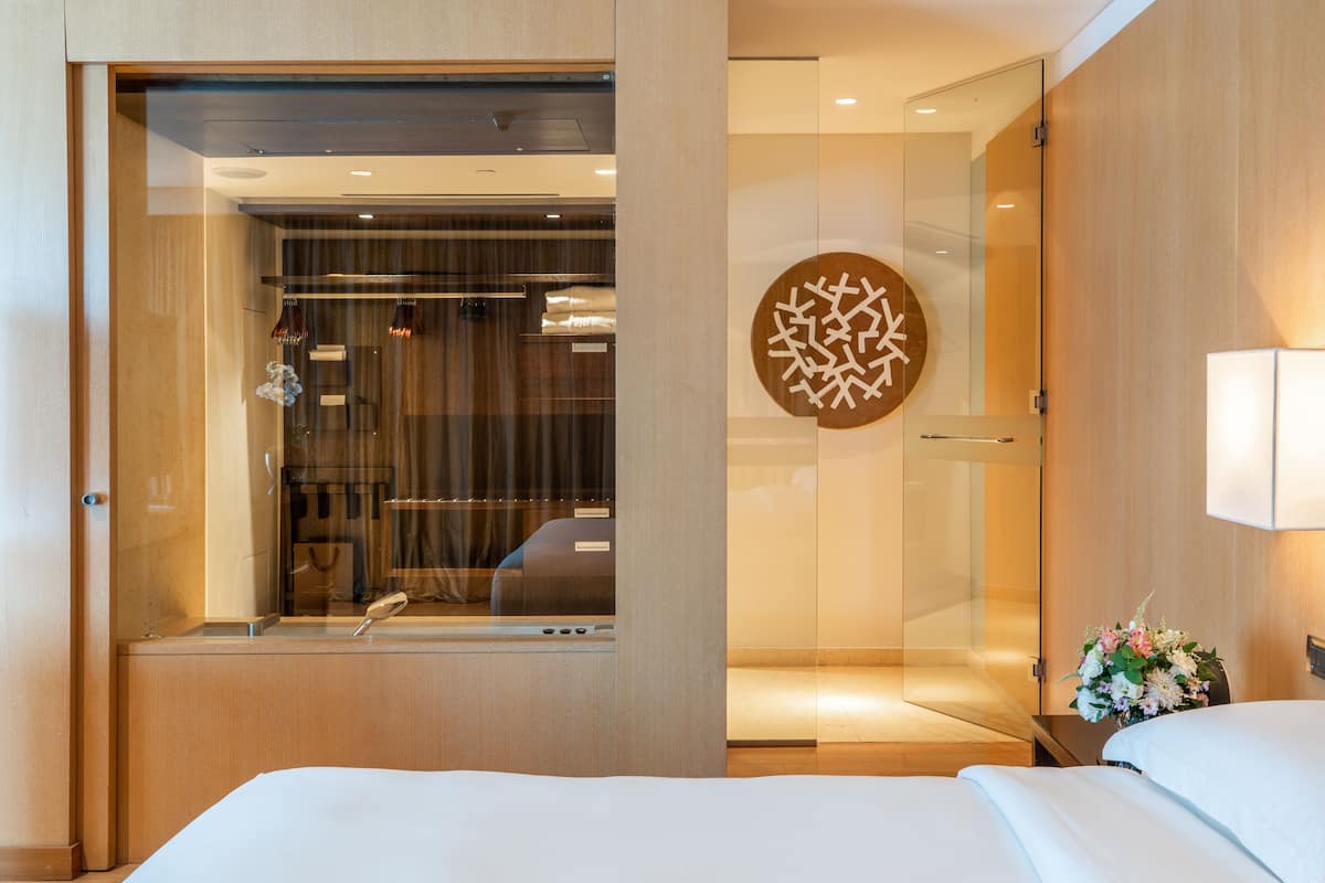 Une chambre d’hôtel avec un grand lit, une douche en verre, un élément décoratif mural et une table de chevet agrémentée d’un vase de fleurs.
