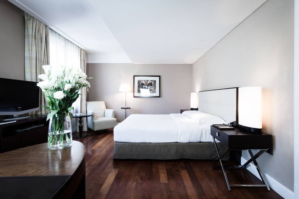 Une chambre d’hôtel avec un lit, des tables de chevet, une télévision et un vase de fleurs.