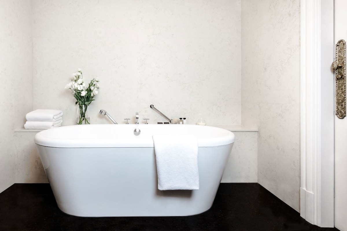 Une salle de bain moderne avec une baignoire sur pieds, un porte-serviettes et un vase de fleurs.