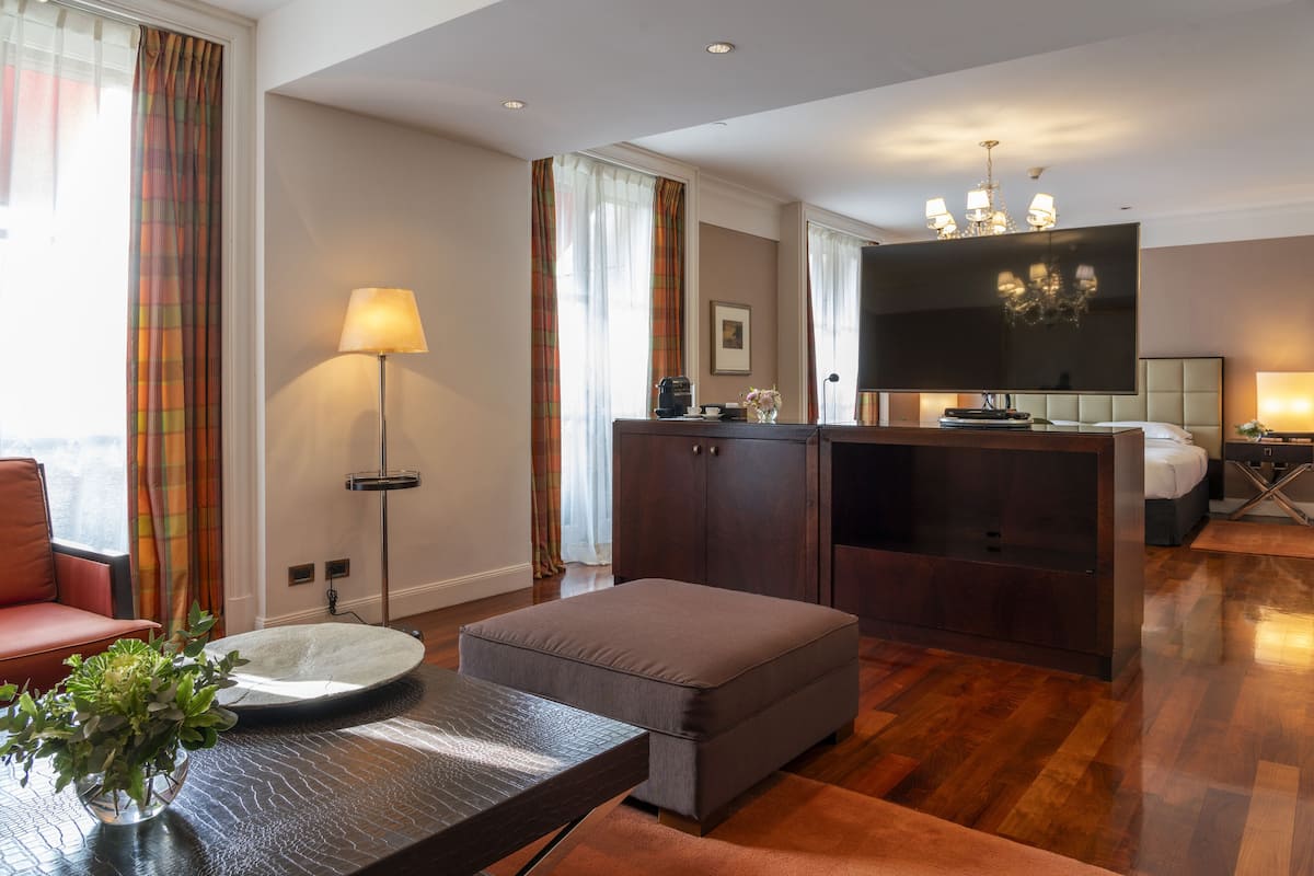 Une chambre d’hôtel moderne équipée d’un canapé, d’un pouf, d’une télévision à écran plat et d’un coin repas avec une table et une lampe.