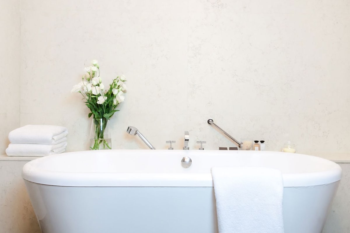 Une salle de bain moderne avec une baignoire sur pieds, un vase en verre contenant des fleurs blanches et des serviettes soigneusement pliées.