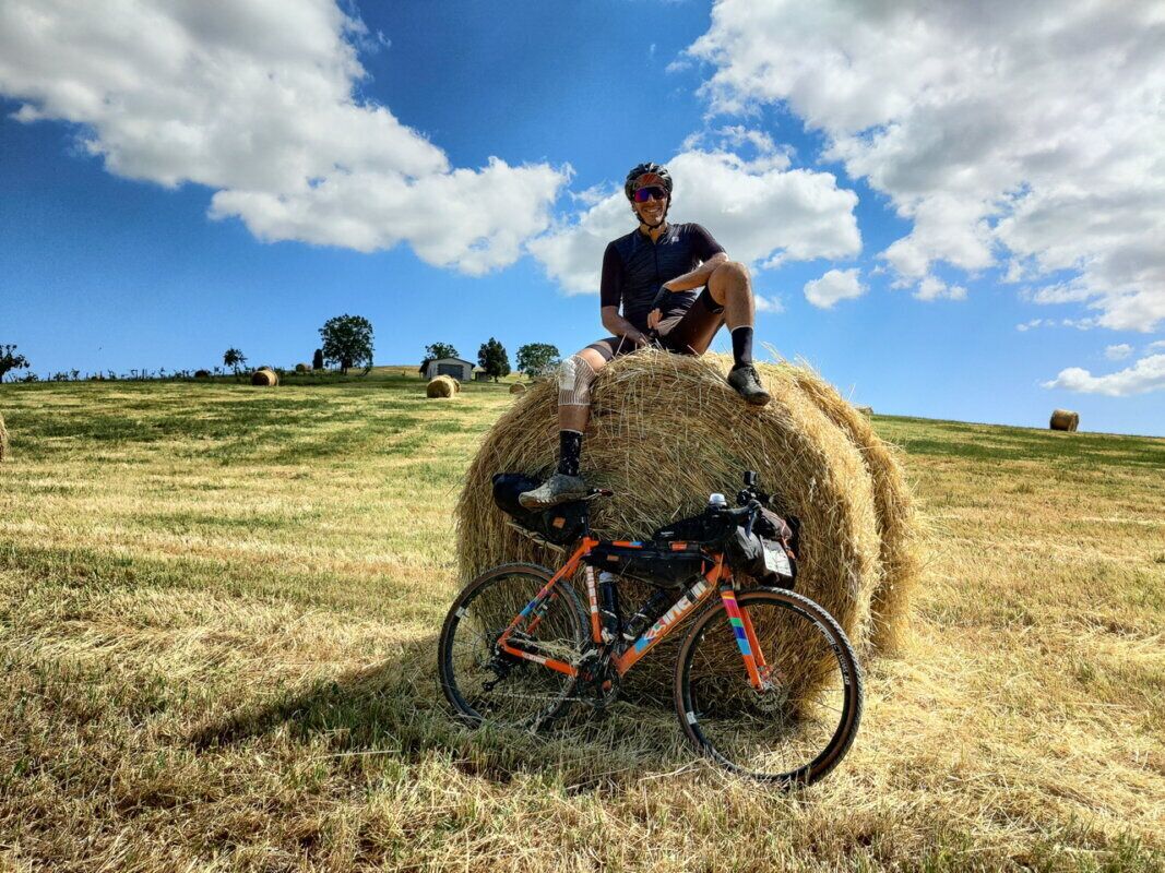 Una persona sentada sobre un fardo de heno con una bicicleta en un campo cubierto de hierba.