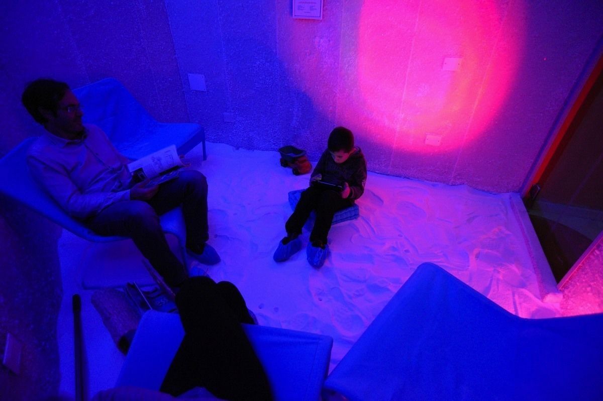A room with a bed, a chair, and a person sitting on the floor.