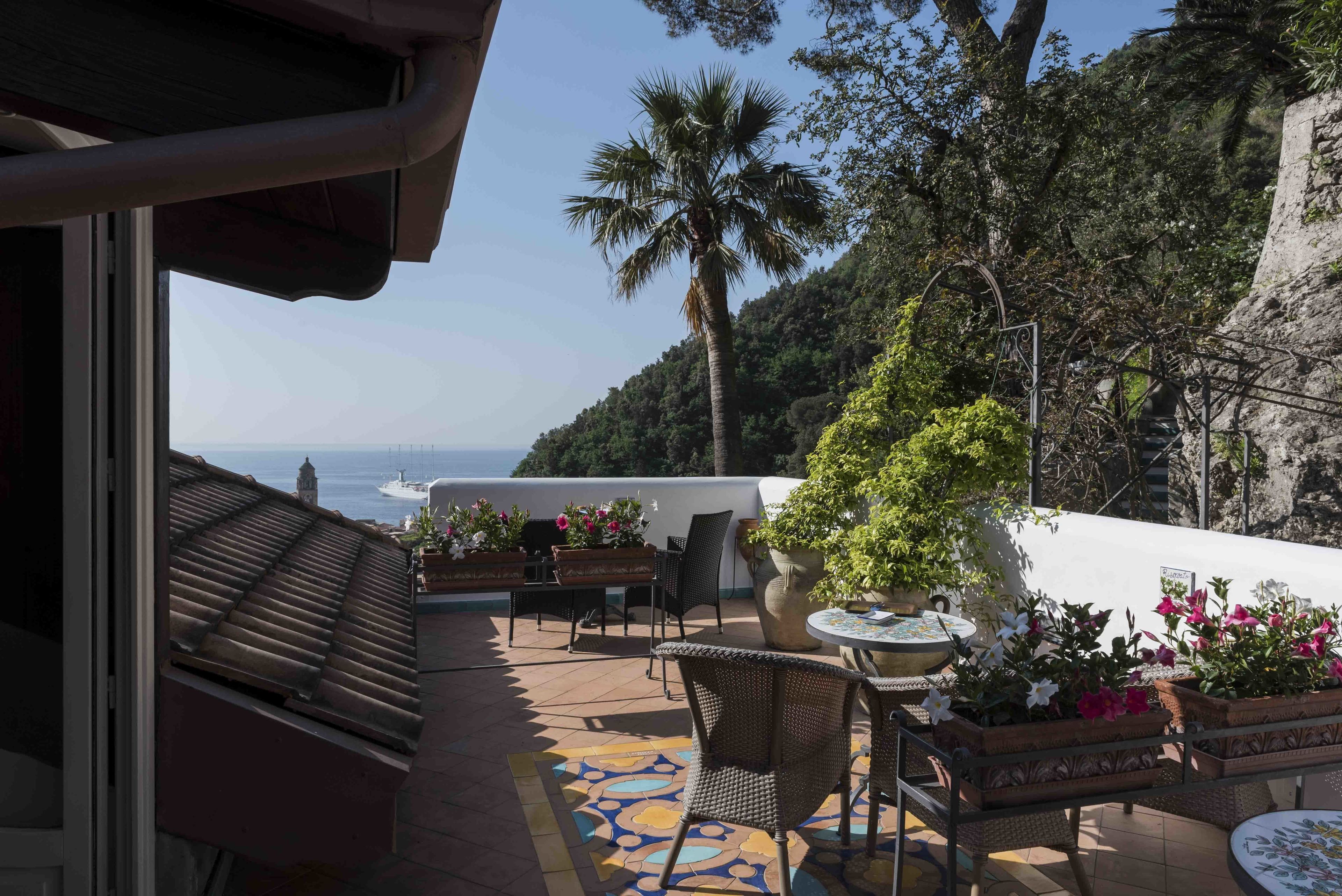 Una terraza con mobiliario exterior, plantas en macetas y vista al mar.