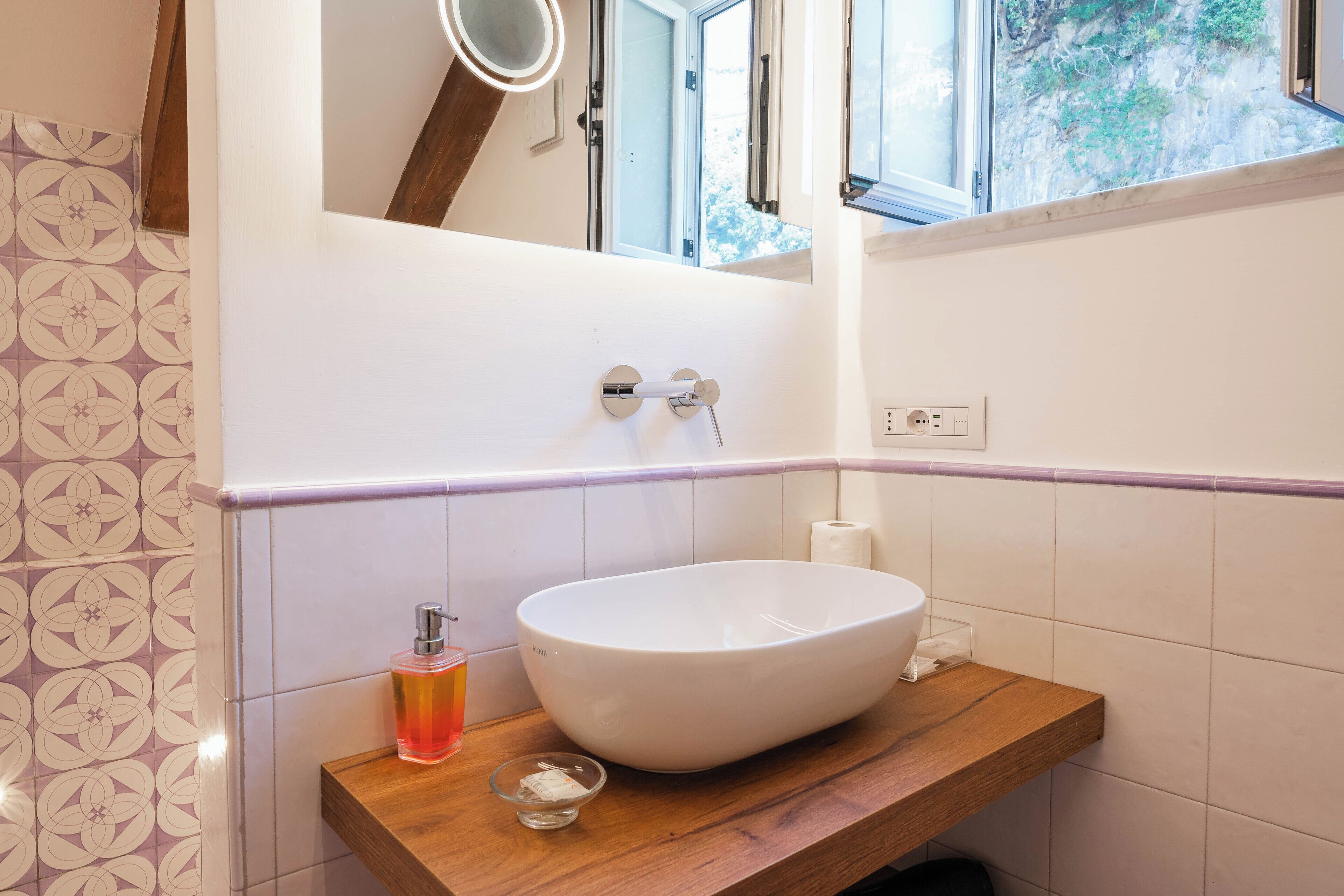 A bathroom with a large white sink, a wooden countertop, a mirror above the sink, and a window with a view of trees.