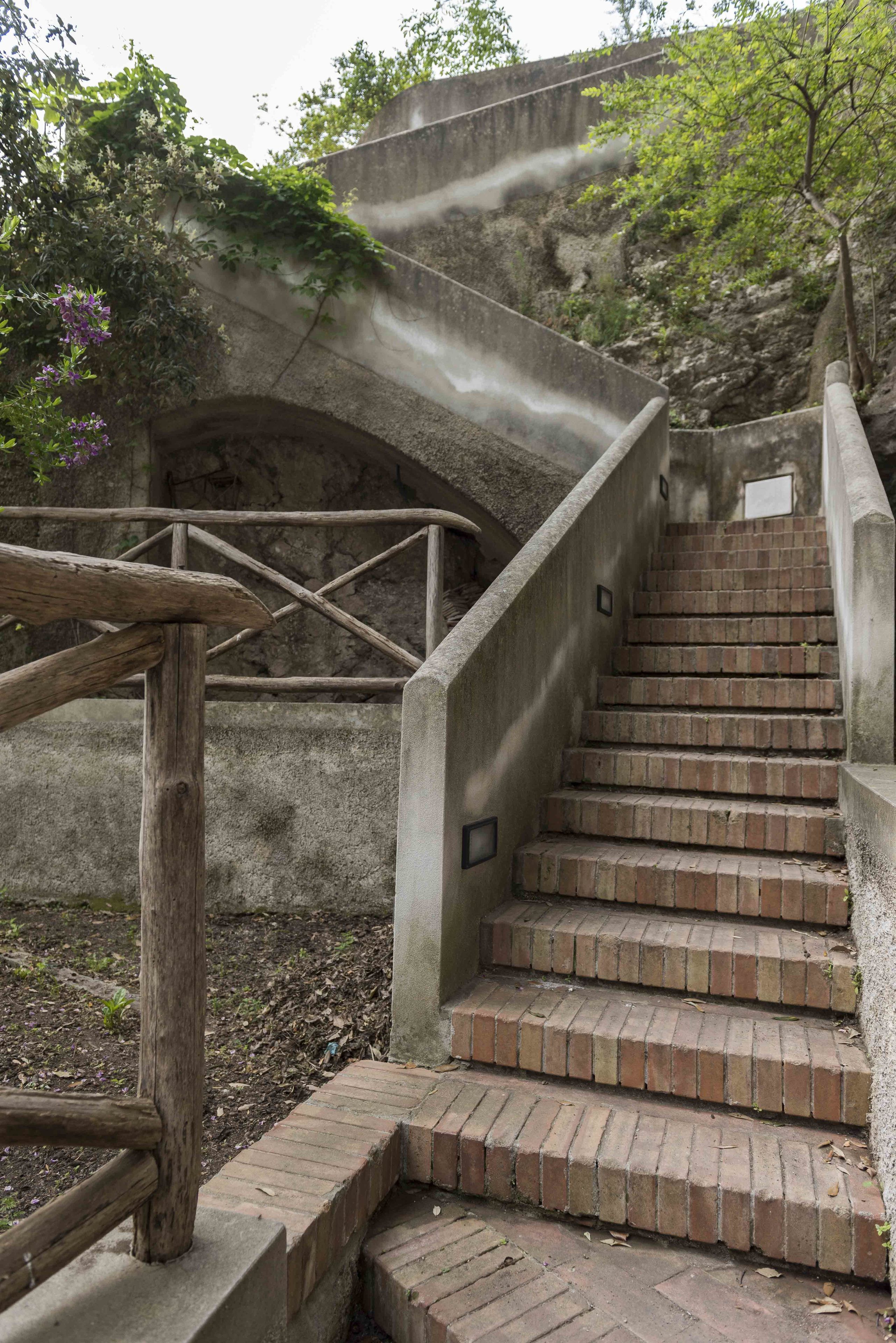 A set of concrete stairs with a wooden handrail, leading up to a stone bridge.