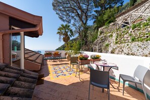 Eine Terrasse mit Sitzgelegenheiten im Freien, Blick auf das Meer und eine Steinmauer.