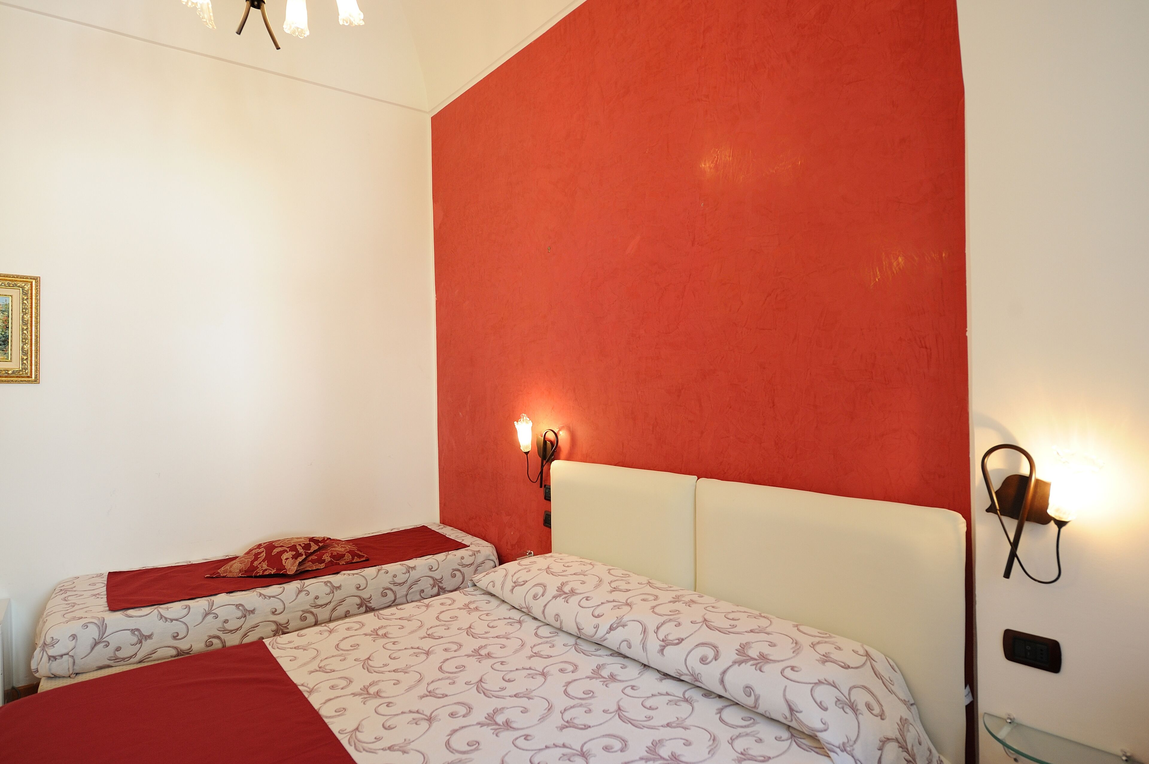 A room with two beds, each with patterned bedding and a red accent.