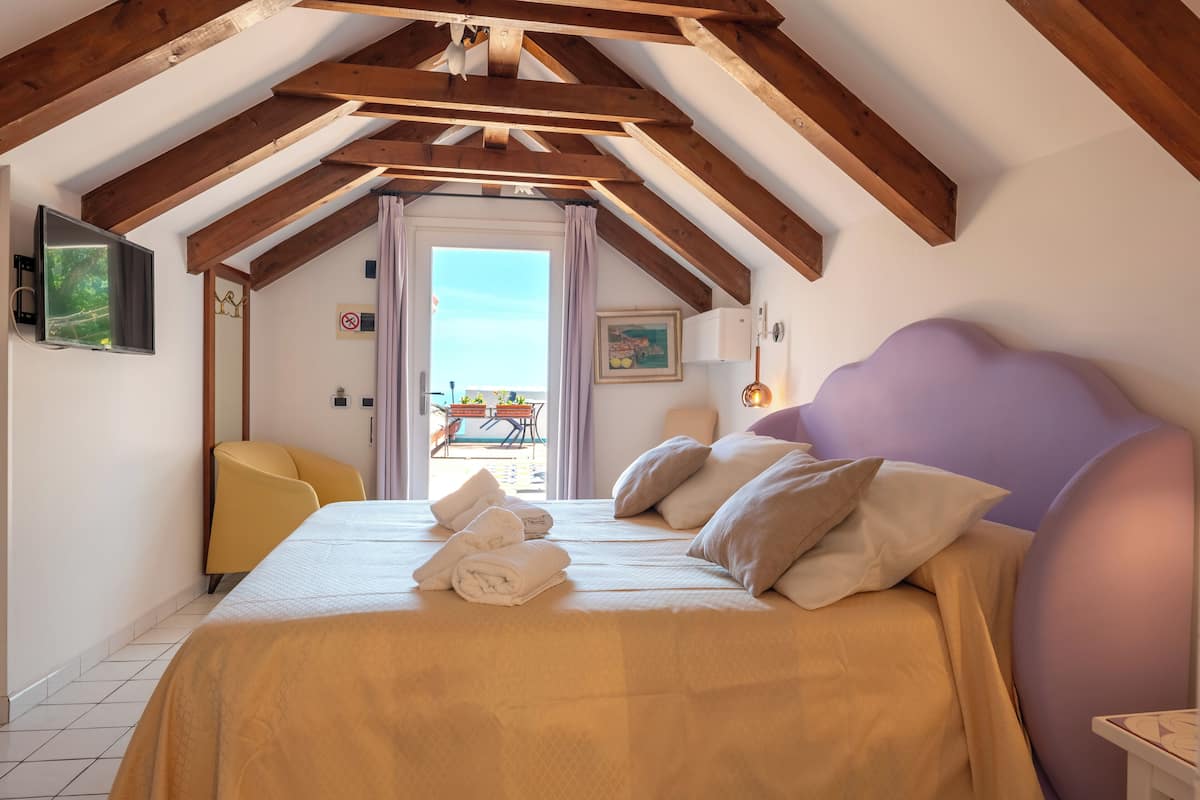 Ein Schlafzimmer mit Bett, Kissen, einem Sessel und einem Fenster mit Vorhängen.