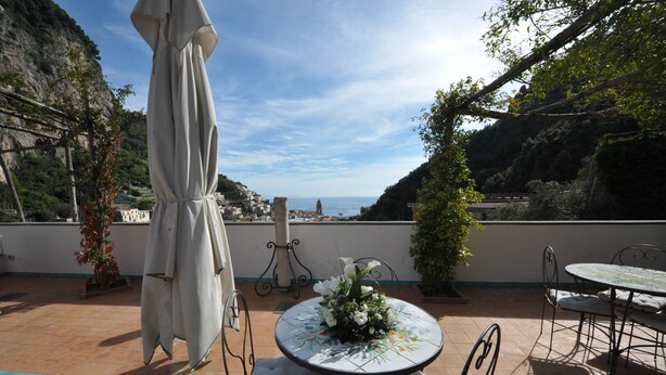 Une terrasse extérieure avec une table ronde et des chaises, un parasol et une vue sur la mer et les collines.