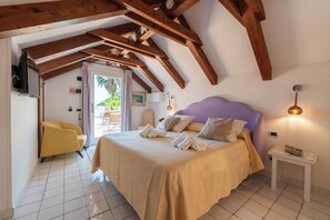 Ein Schlafzimmer mit einem großen Bett, Holzbalken, einem kleinen Tisch, einem Stuhl und Blick ins Freie.