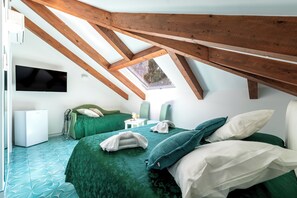 Une chambre avec un plafond en pente, un téléviseur à écran plat, un lit avec une literie verte, une petite table et une chaise.
