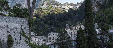 Une ville côtière où les bâtiments sont adossés à une falaise, protégés par un mur de pierre, et où la végétation luxuriante abonde.