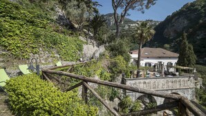 Un bâtiment historique, doté d’un toit recouvert de tuiles, entouré d’une végétation luxuriante et auquel on accède par un escalier en pierre.
