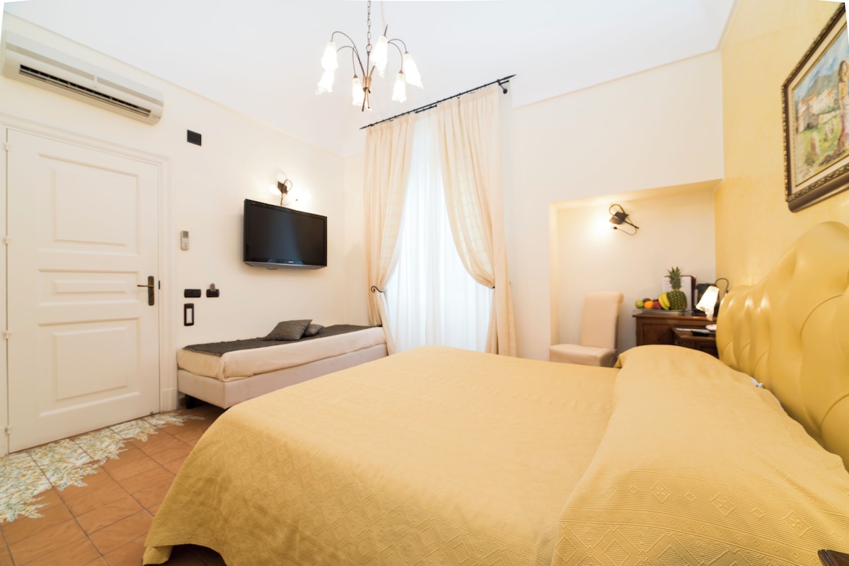 Une chambre à coucher avec un lit, un téléviseur fixé au mur, une chaise et une petite table sur laquelle se trouvent des fruits.