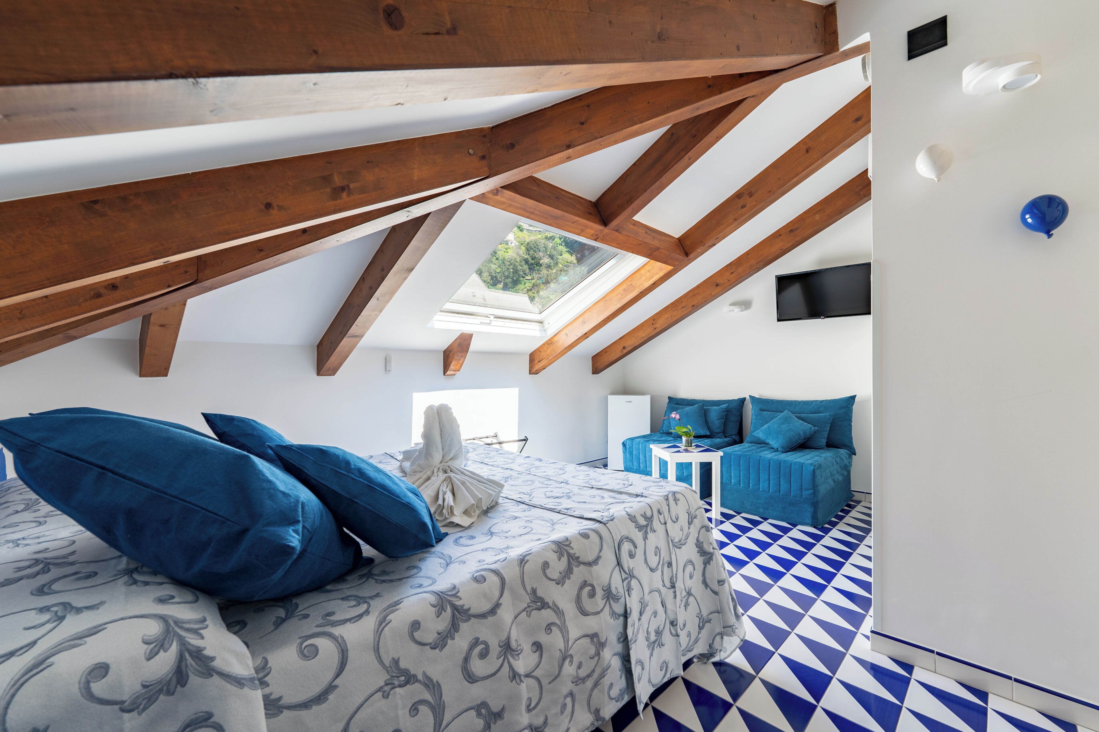 A bedroom with a skylight, a bed with patterned bedding, a blue sofa, and a checkered floor.