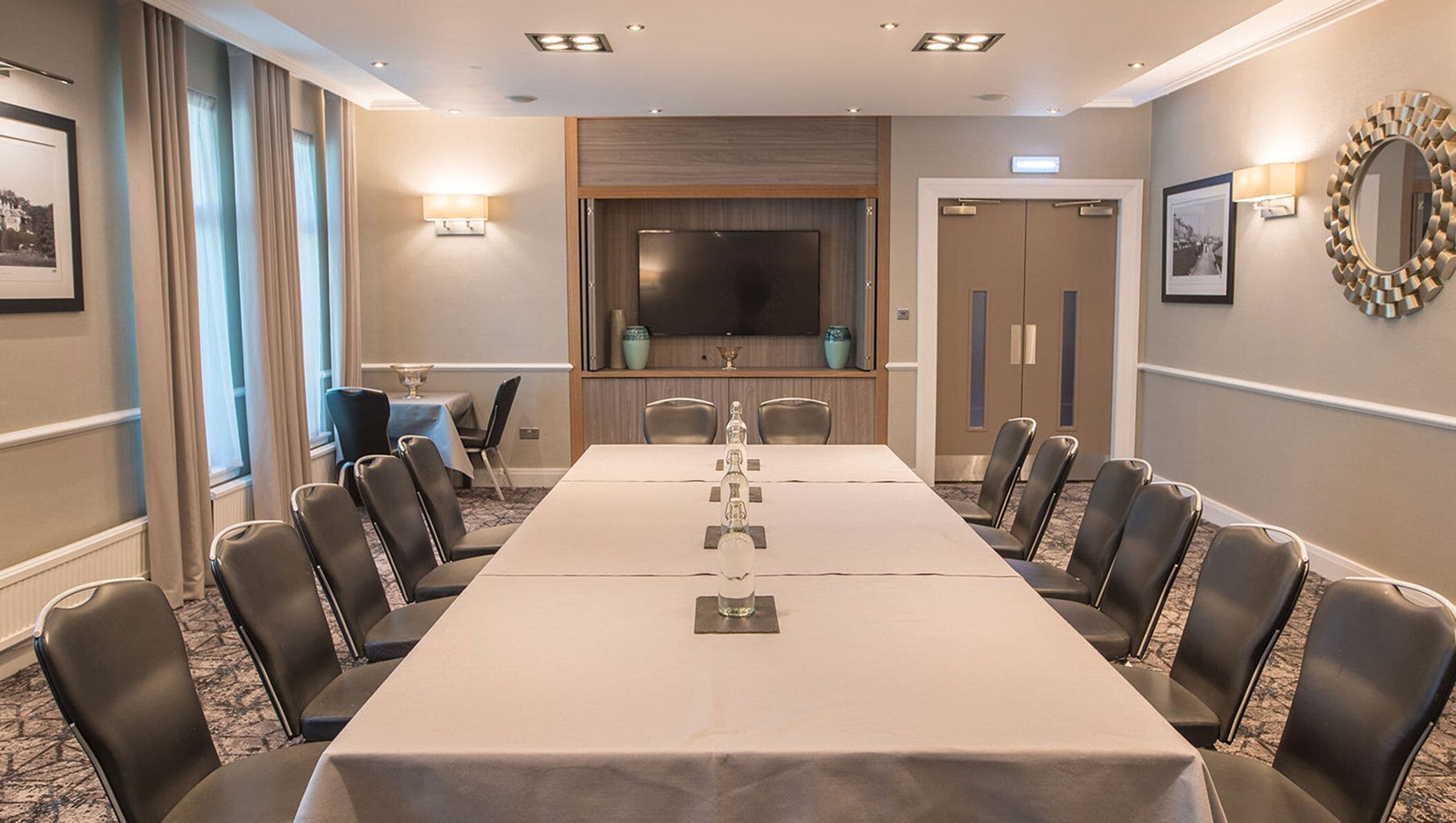 A conference room with a long table, chairs, a television, and a decorative mirror.