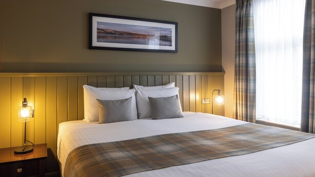 A neatly made bed with a plaid throw, a framed picture on the wall, and bedside lamps.