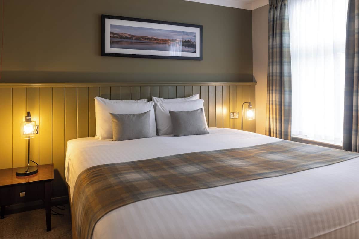 A neatly made bed with a plaid throw, a framed picture on the wall, and bedside lamps.