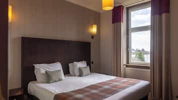 Une chambre d’hôtel avec un grand lit, deux tables de chevet, une fenêtre avec des rideaux et des lampes fixées au mur.
