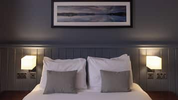 Uma cama bem arrumada com duas almofadas, um quadro emoldurado acima e duas luminárias fixadas nas paredes, uma de cada lado.