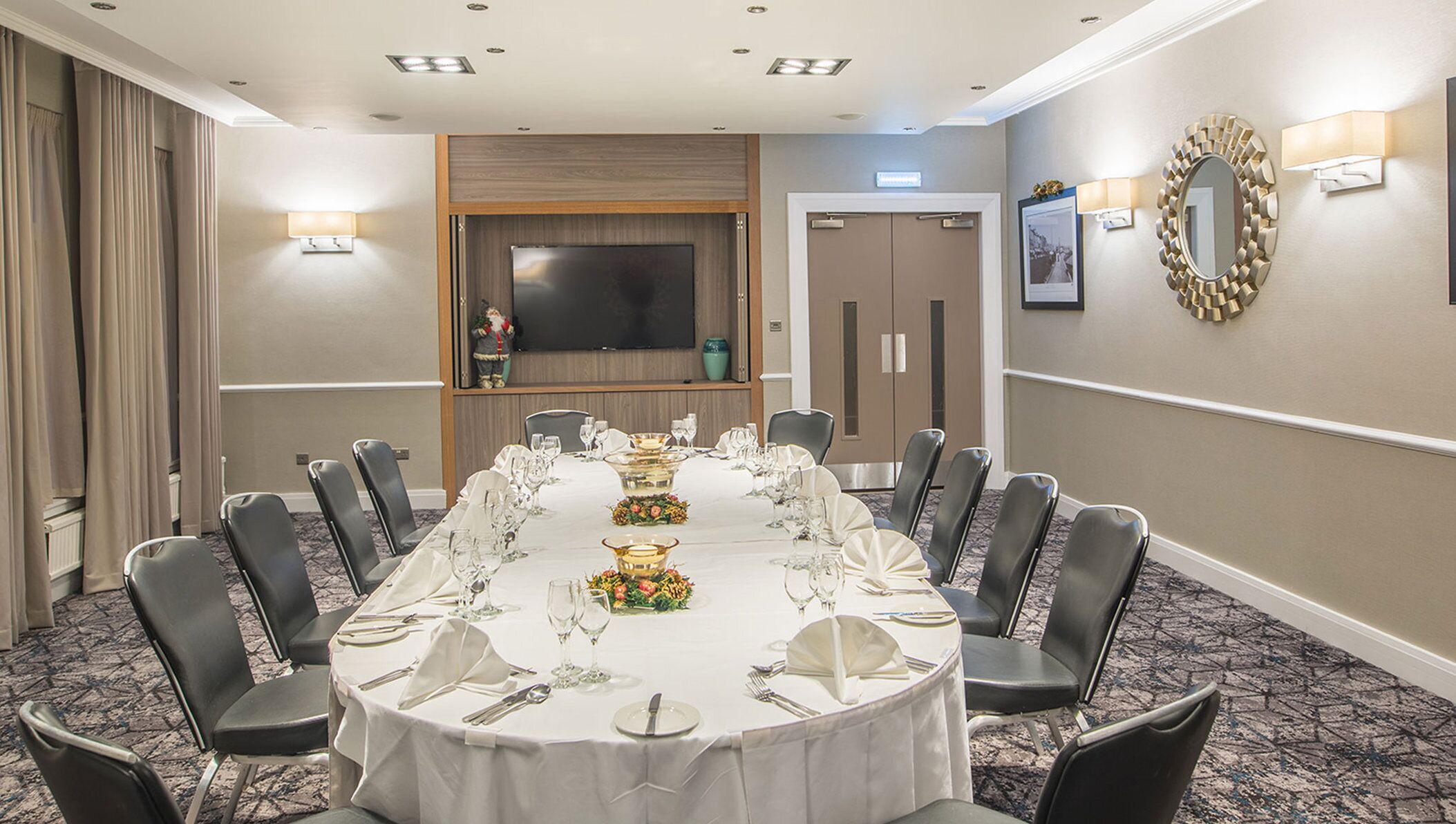 A conference room with a long table set for a formal event, equipped with chairs, a television, and a mirror on the wall.