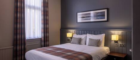 A hotel room with a large bed, two bedside lamps, a framed picture on the wall, and a window with curtains.