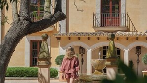 Una mujer caminando frente a un edificio con una fuente y un balcón.