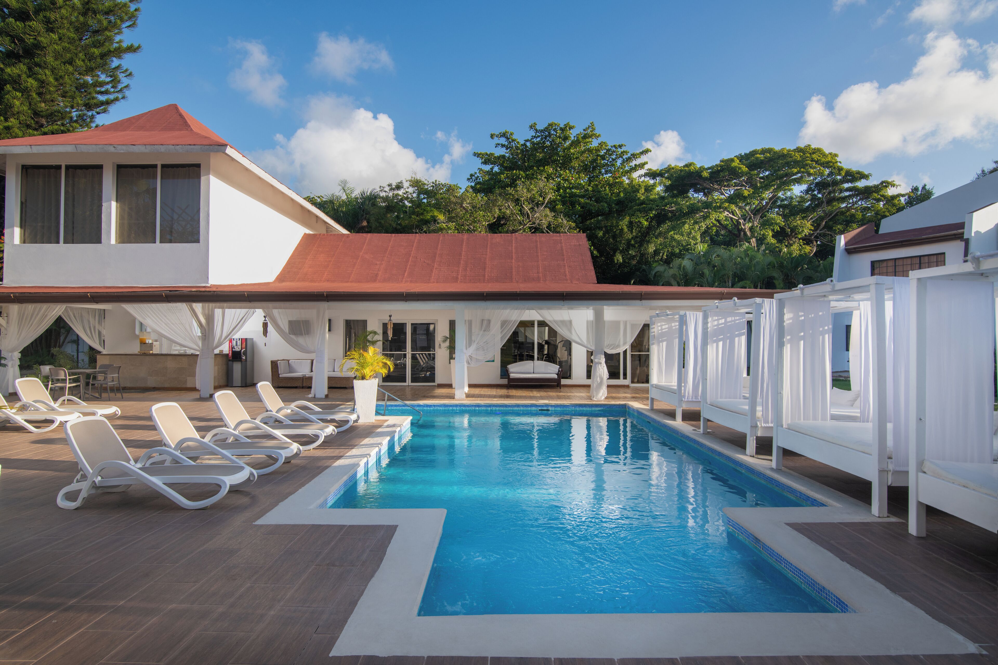 A swimming pool with lounge chairs, a covered seating area, and a building with a red roof.