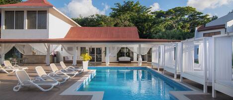 A swimming pool with lounge chairs, a covered seating area, and a building with a red roof.