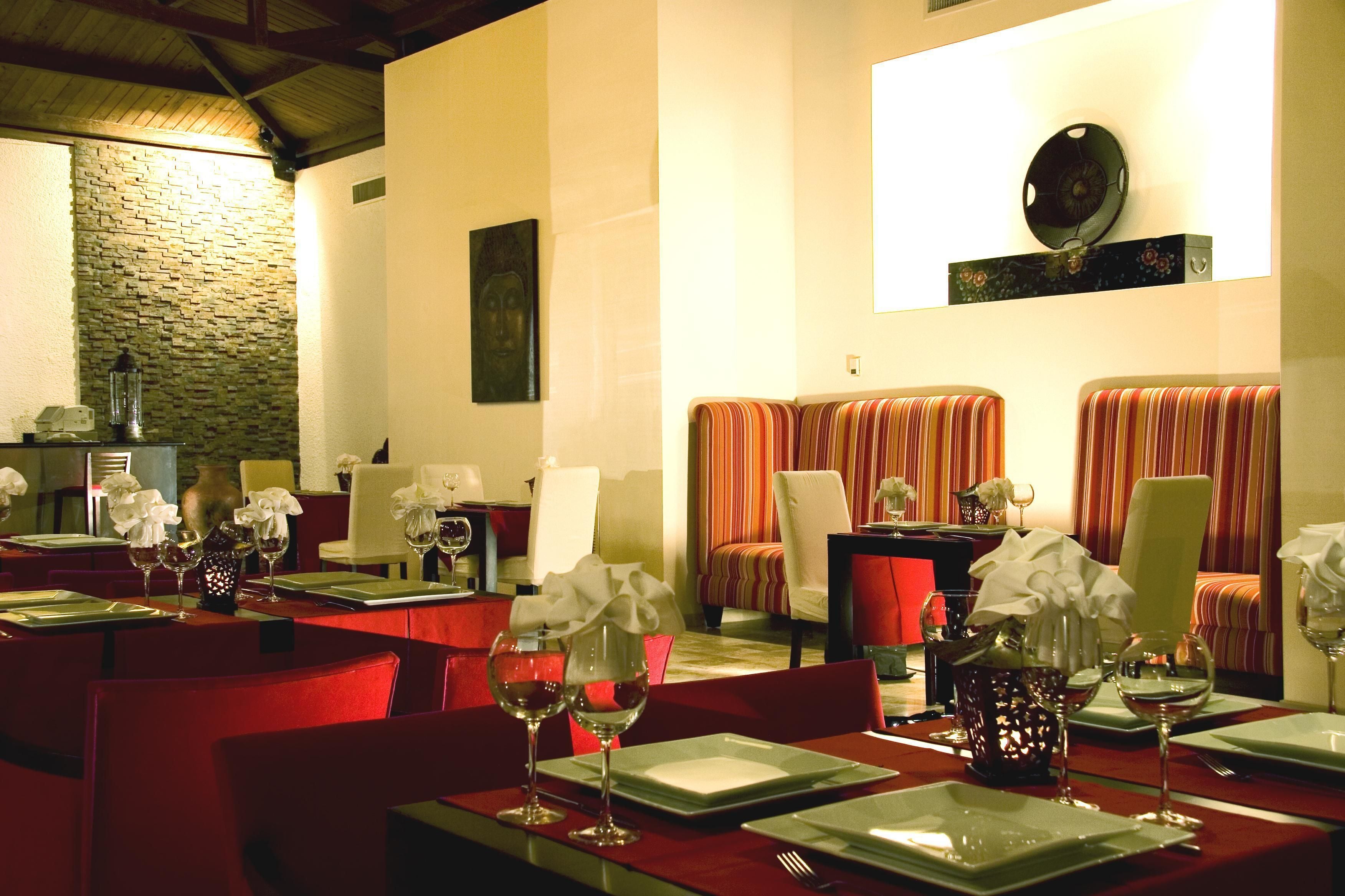 Un comedor con sillas tapizadas en rojo, vajilla blanca y una pared de piedra.