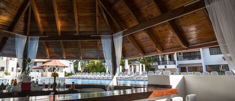 A wooden ceiling with a pool view, white chairs, and a bar area.