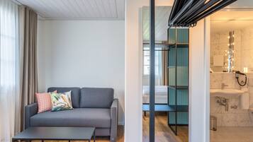 A modern room with a grey sofa, a small table, and a bathroom with a mirror, sink, and shower.