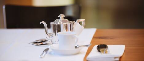 Une table dressée avec une théière, une tasse, une soucoupe et une cuillère, ainsi qu’une serviette et un verre posés sur la table.
