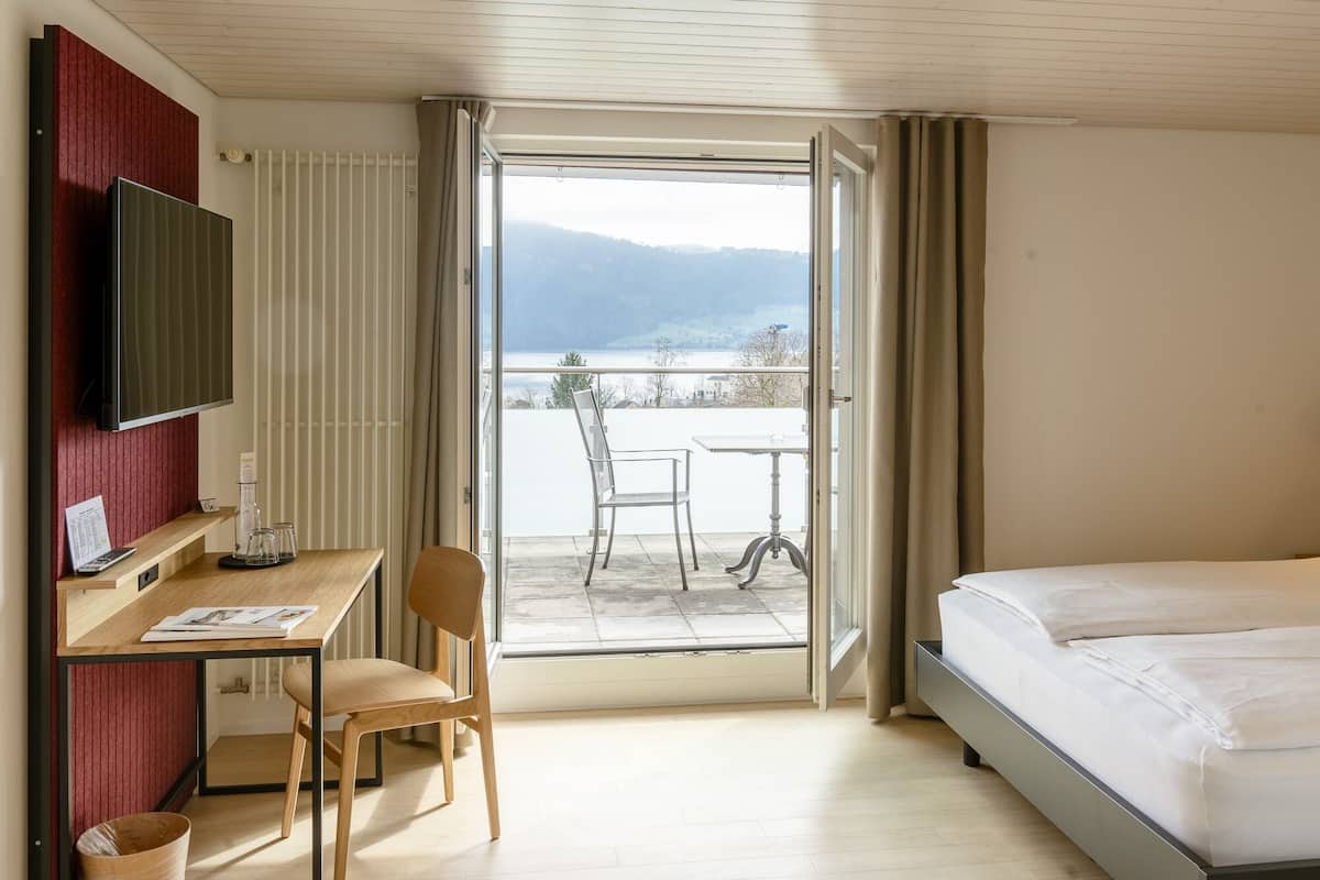 A hotel room with a bed, a desk with a chair, a TV, and a balcony with a table and chair.