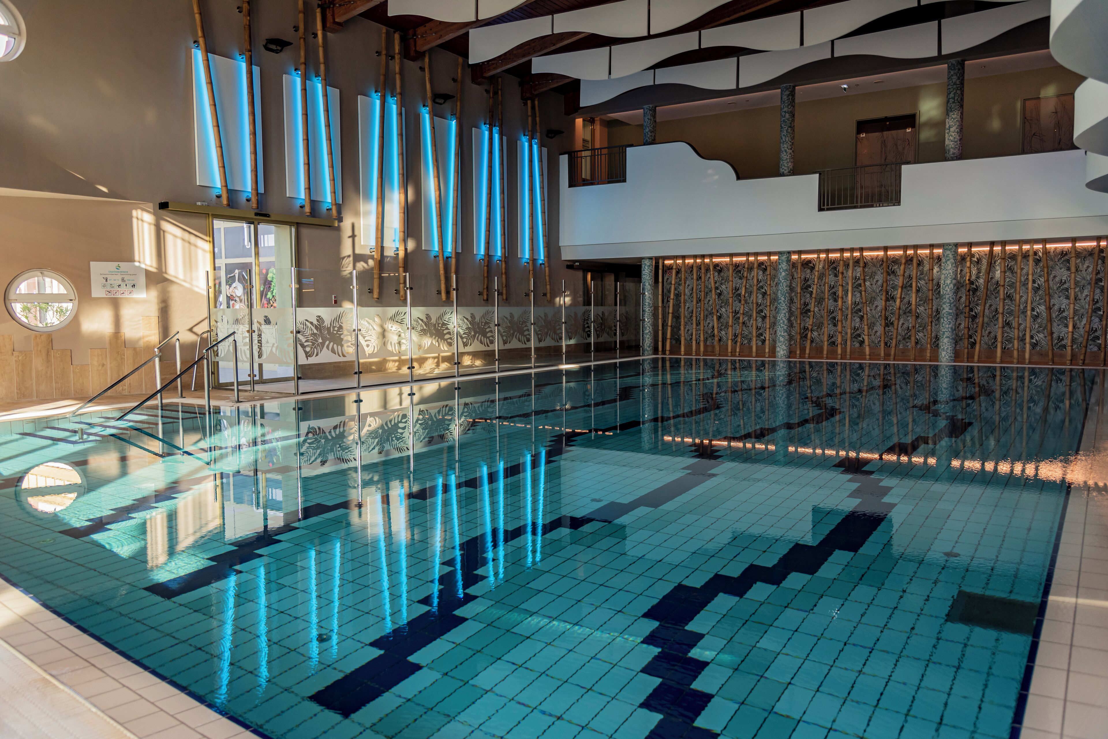An indoor swimming pool with clear water, glass railings, and a tiled floor.