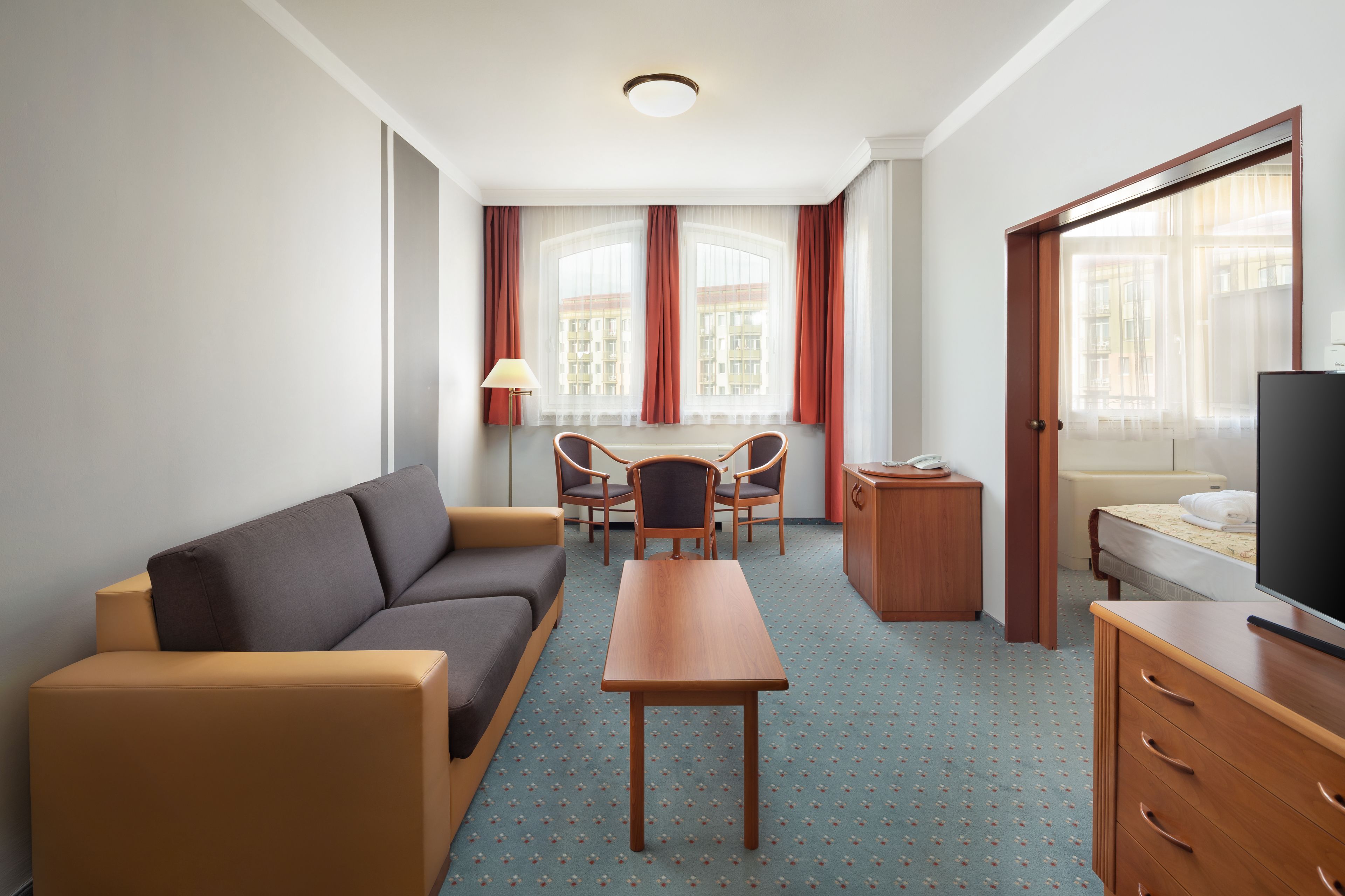 A hotel room with a sofa, a dining table with chairs, a TV, and a bed.