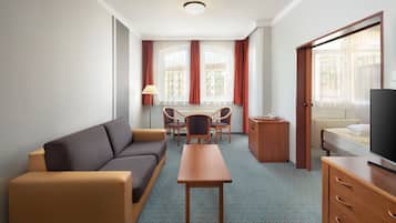 A hotel room with a sofa, a dining table with chairs, a TV, and a bed.
