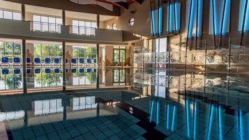 Una piscina interior amplia con paredes de vidrio transparente, sillas azules y diseño moderno.